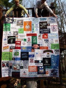 2 women holding a T-shirt quilt over the railing of a deck. 