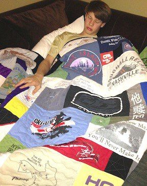 A young man sleeping under a T-shirt quilt on a couch.