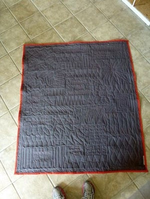 This is the back of a T-shirt quilt photographed on the tile floor.